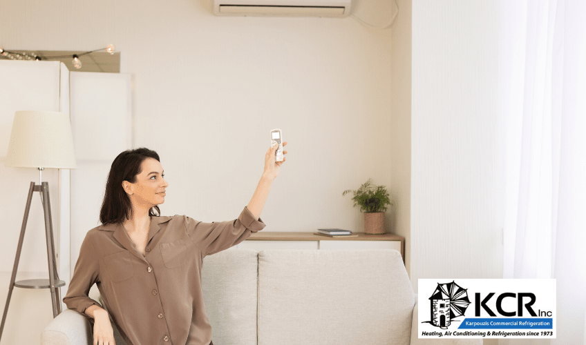 Woman at home on couch adjusting air conditioner for best temperature with remote control.