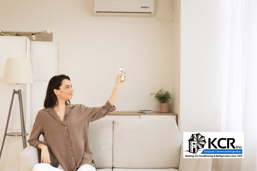 Woman at home on couch adjusting air conditioner for best temperature with remote control.