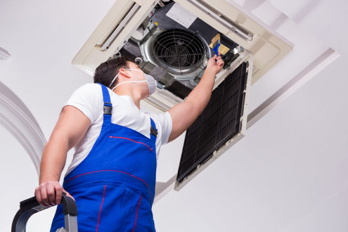 Worker repairing ceiling air conditioning unit Worker repairing ceiling air conditioning unit